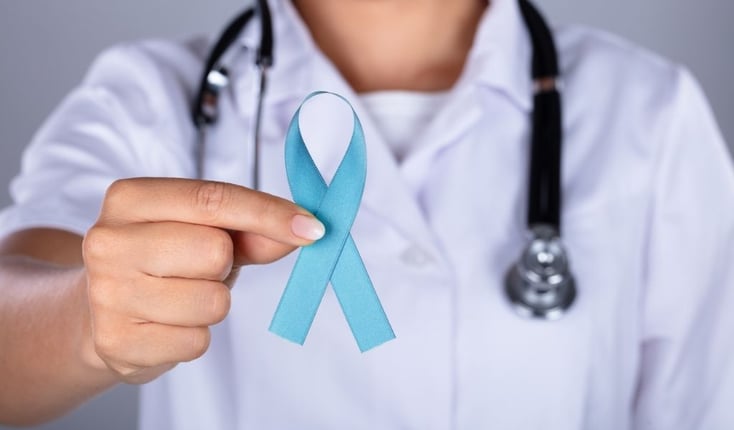 A doctor's hand holding the ribbon for ovarian cancer